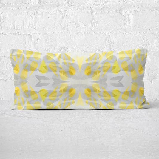 Rectangular lumbar pillow featuring an abstract hand-painted pattern in yellow and grey tones leaning against a white brick wall.