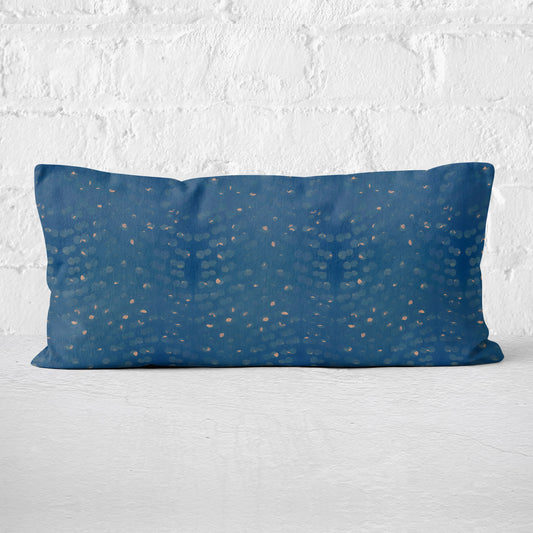 Rectangular lumbar pillow with hand-painted blue and beige pattern against a white brick wall.