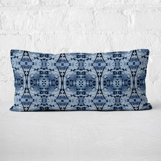 Rectangular lumbar pillow featuring an abstract hand-painted pattern in blue and black India Ink leaning against white brick wall