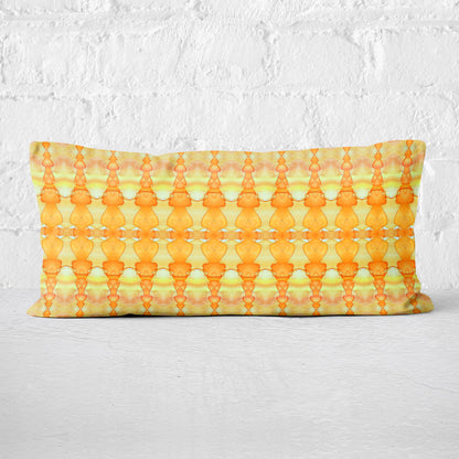 Rectangular lumbar pillow featuring abstract hand-painted yellow and orange pattern leaning against a white brick wall.